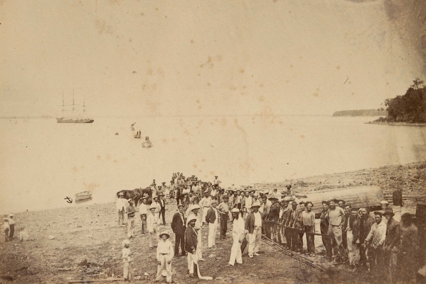 A black and white photo of dozens of people landing an underwater sea cable.