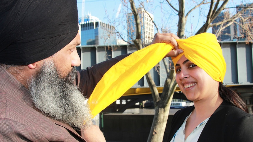 Amar Singh, wearing a black turban, ties a bright yellow turban on a woman.