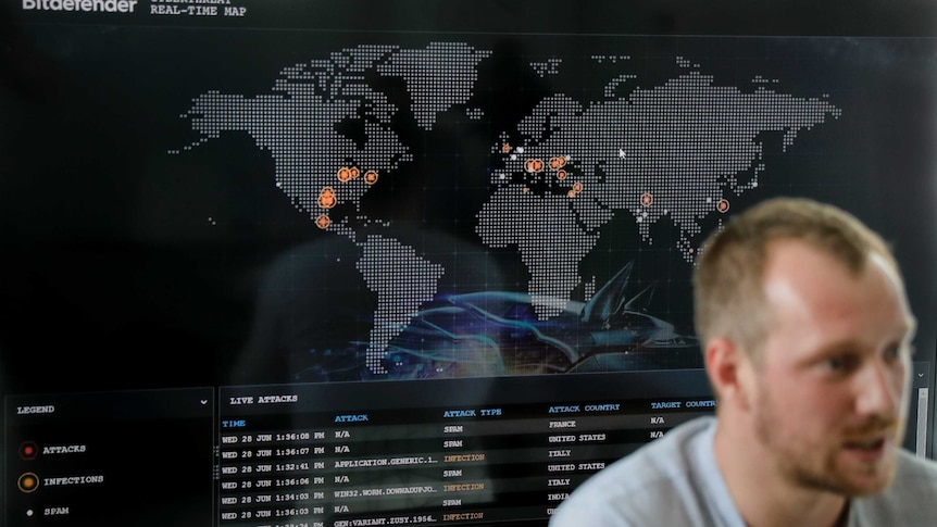 A cyberthreats specialist speaks with reporters with a digital screen behind him.