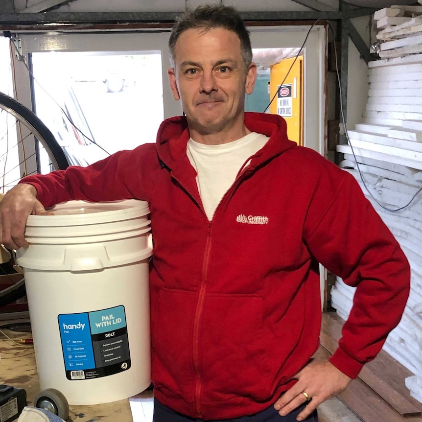 A man stands with his hand on a bucket.