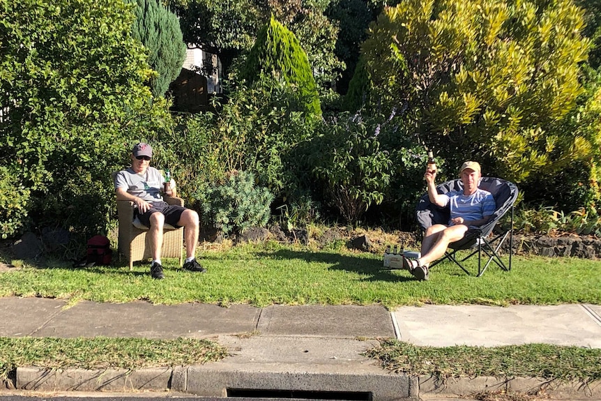 Two men sit in chairs with beers in hand