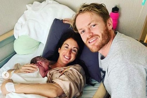 Woman laying in a hospital bed holding her baby after giving birth, with her husband staying beside the bed