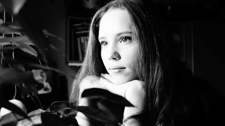 A black and white image of a teenage girl gazing out a window