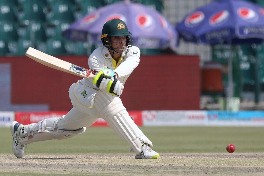 Alex Carey plays a sweep shot while wearing cricket whites