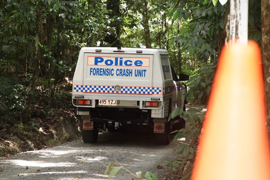 A forensic crash unit police car drives on a sandy path in thick canopy.