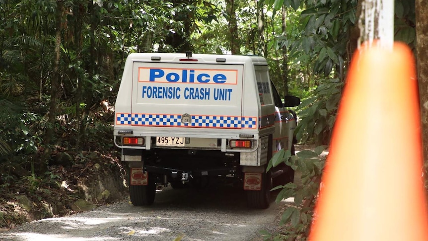 A forensic crash unit police car drives on a sandy path in thick canopy.