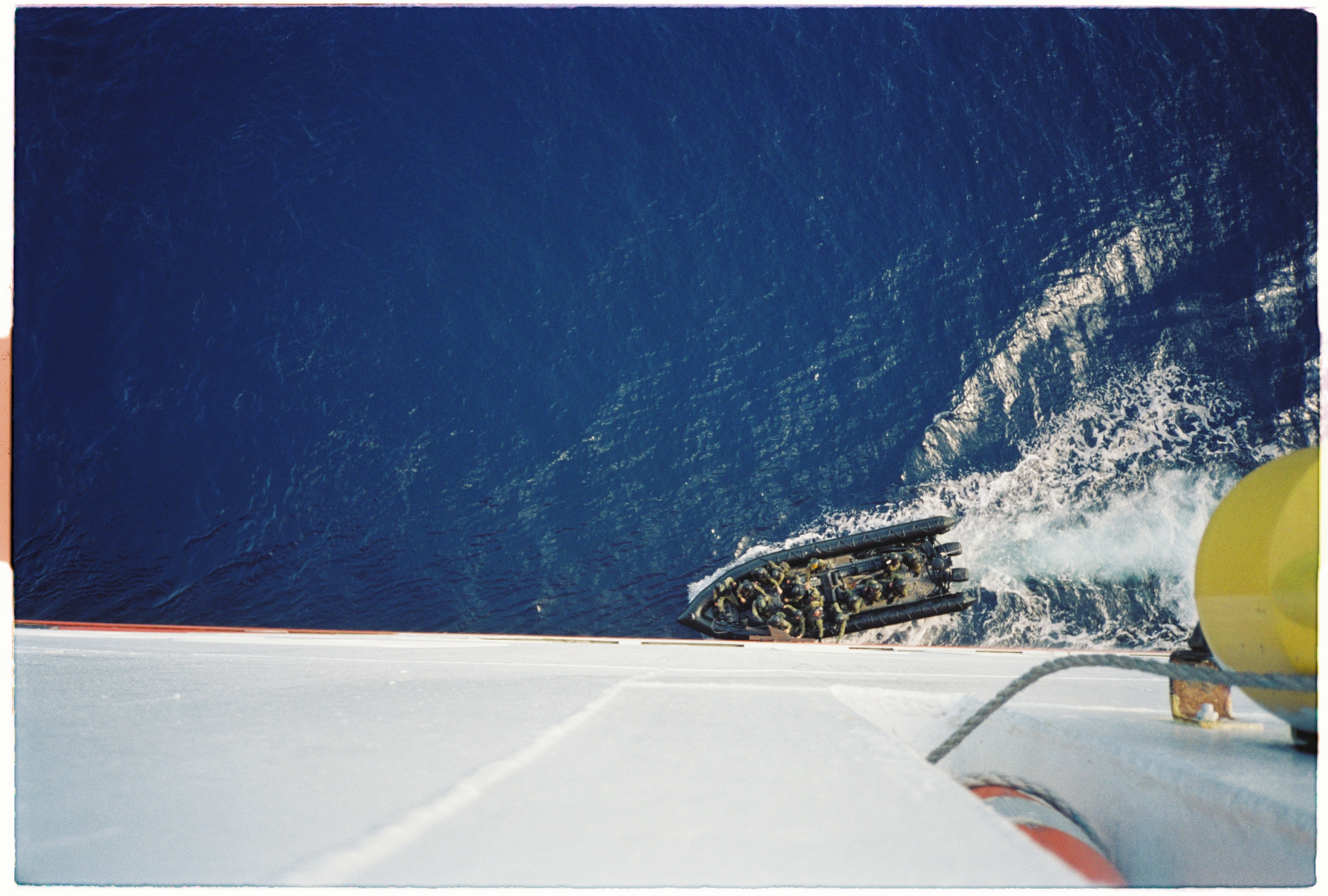 An inflatable military vessel draws close to the side of a large freighter.