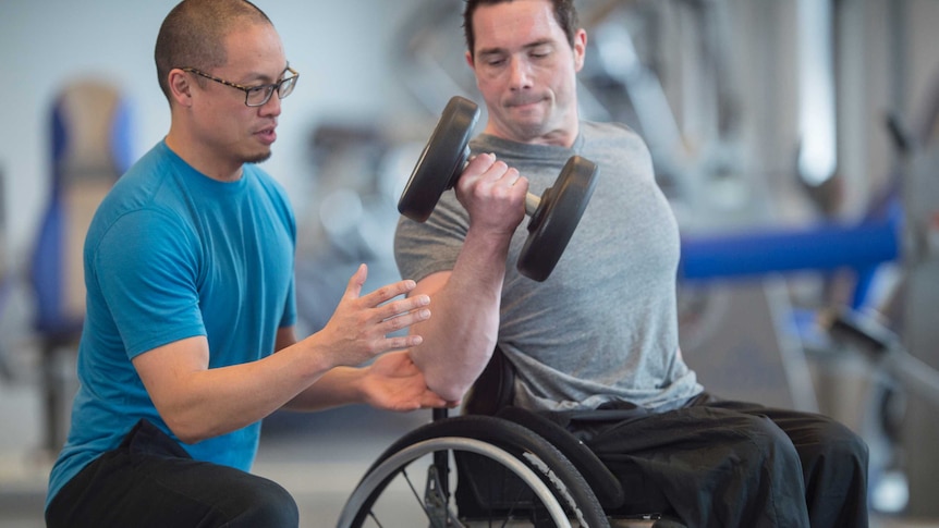 Personal trainer instructing man in wheelchair on lifting weights