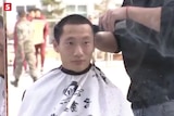 A young man sits down, wearing a cape as he gets a haircut.