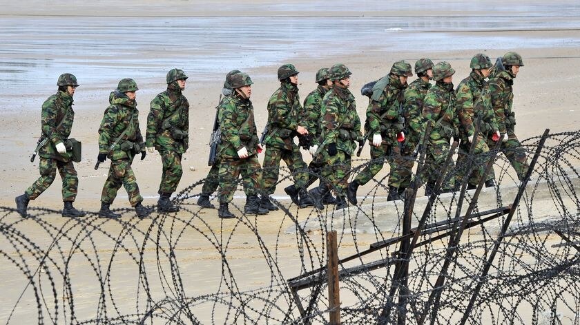 South Korean soldiers march past barbed wire on a beach