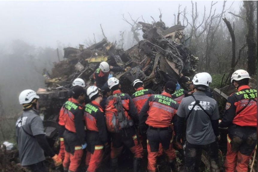 A crowd of rescue workers look at the wreckage of a Black Hawk helicopter in foggy scrubland.