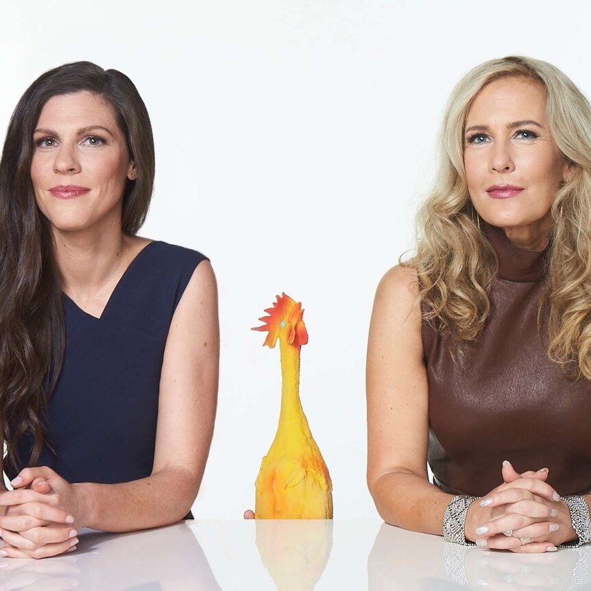 two women looking into the camera with a rubber chicken between them