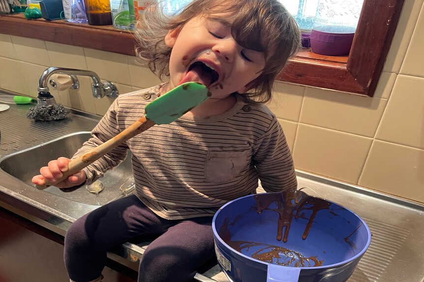 a young girl licks cake batter
