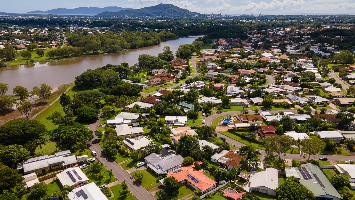 La vista de las casas de las casas que bordean una orilla del río marrón en un día soleado con montañas en la distancia.