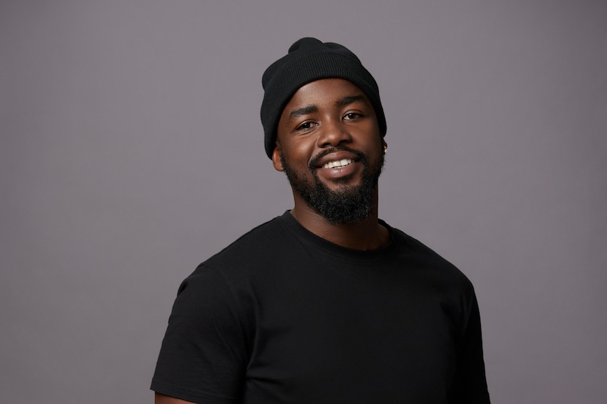 A black man wearing a beanie and black shirt. He has a beard and moustache