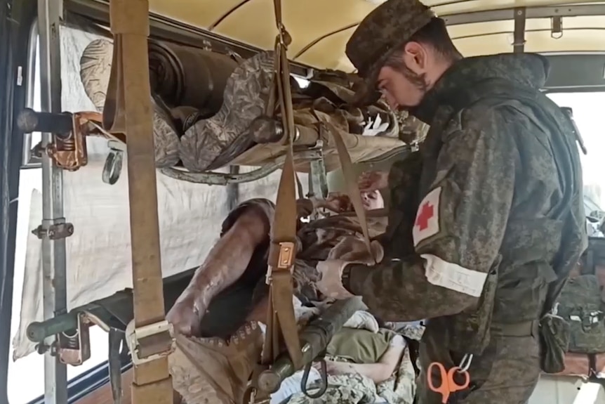 A man tends to wounded people lying in in hammocks on a bus.