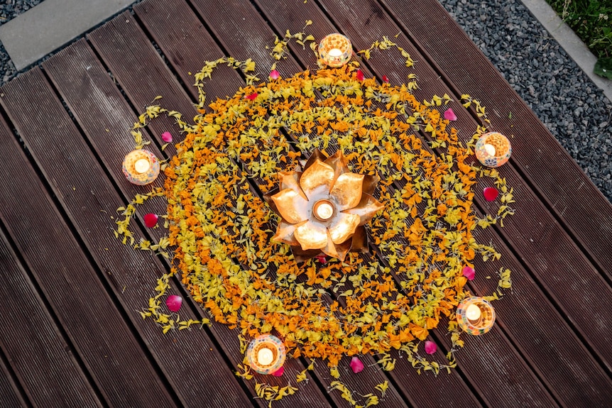A rangoli design made up of colourful powder, flowers, rice and clay lamps.