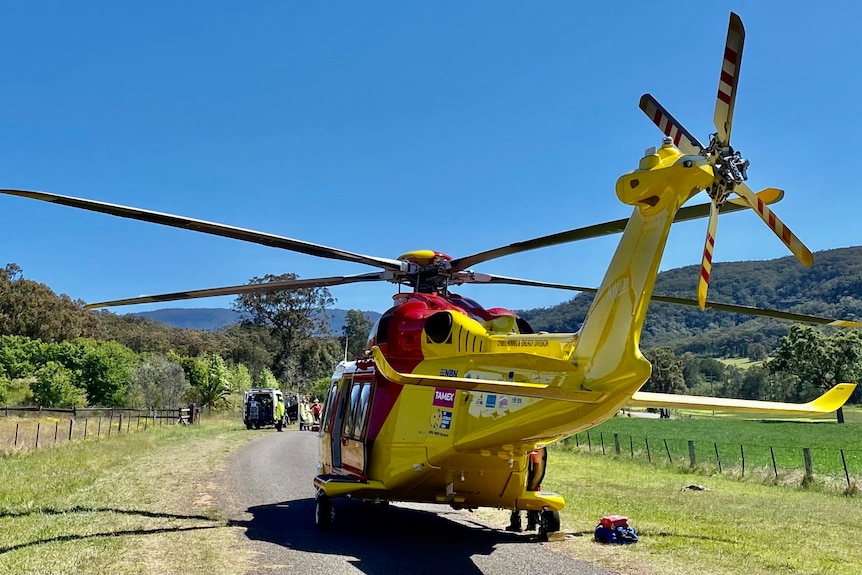 A yellow and red helicopter landed on a country road