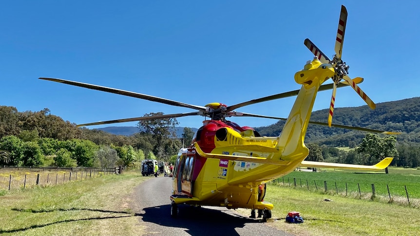 A yellow and red helicopter landed on a country road.