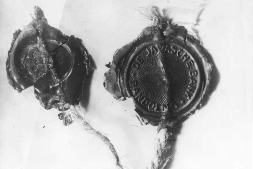 A black and white photo of two wax seals on a piece of string. One has a the words "De Javasche Bank" on it.