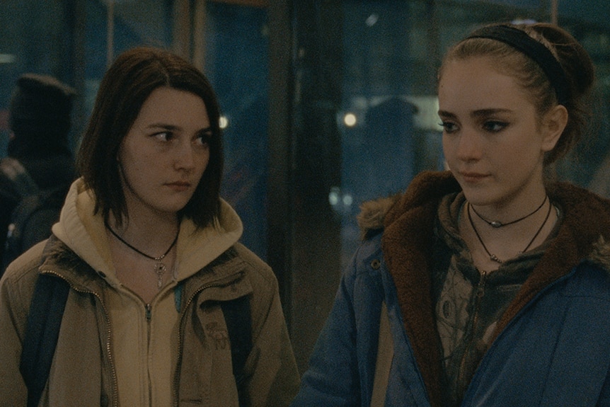 Autumn (Sidney Flanigan) looking at her cousin Skylar (Talia Ryder). Both are dressed for the cold in heavy jackets.