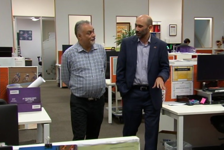 Two men walking next to each other through an office