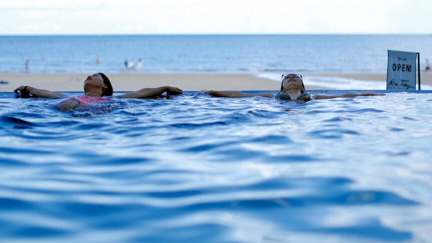 Two women lounging in a pool overlooking a Thai beach