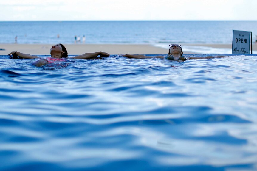 Two women lounging in a pool overlooking a Thai beach