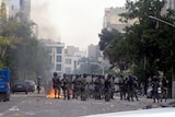 Iranian riot police stand in front of flames in Enghelab Square, Tehran