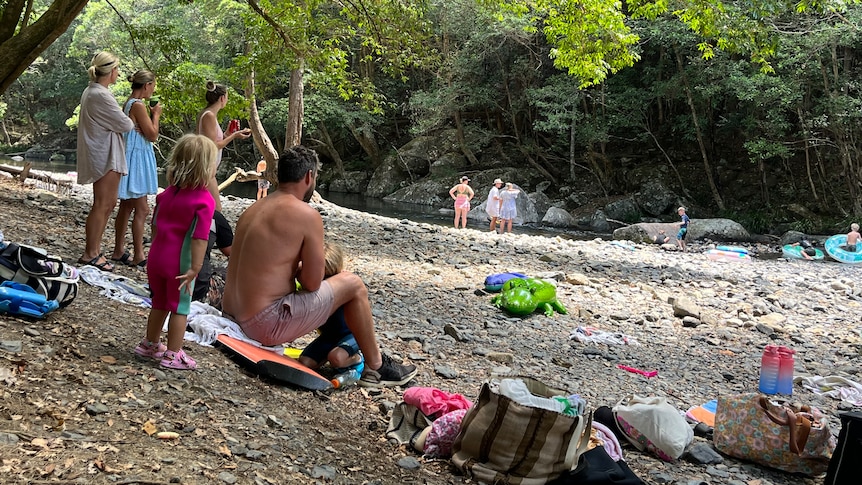 A group of people including three women, a toddler and man watch people playing in the river