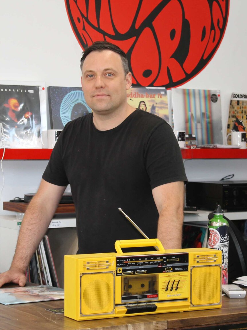 Dylan Sainsbury standing behind a yellow cassette player at his shop, Rhubarb Records in Perth