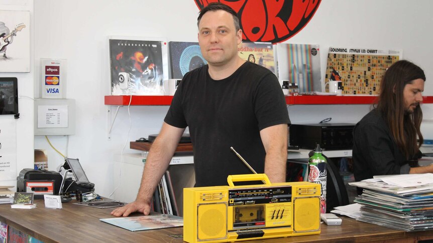 Dylan Sainsbury standing behind a yellow cassette player at his shop, Rhubarb Records in Perth