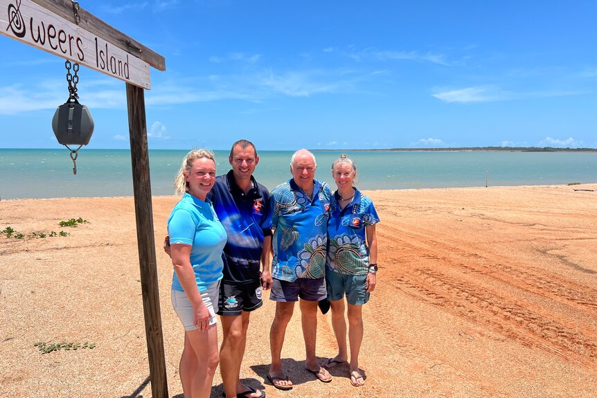 four people wearing blue shirts stand on a beach smiling