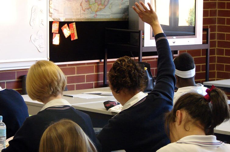 A student sits in a classroom with her hand raised.