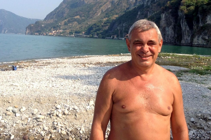 Oleg Kouzmine stands on a white pebble beach without a shirt on.