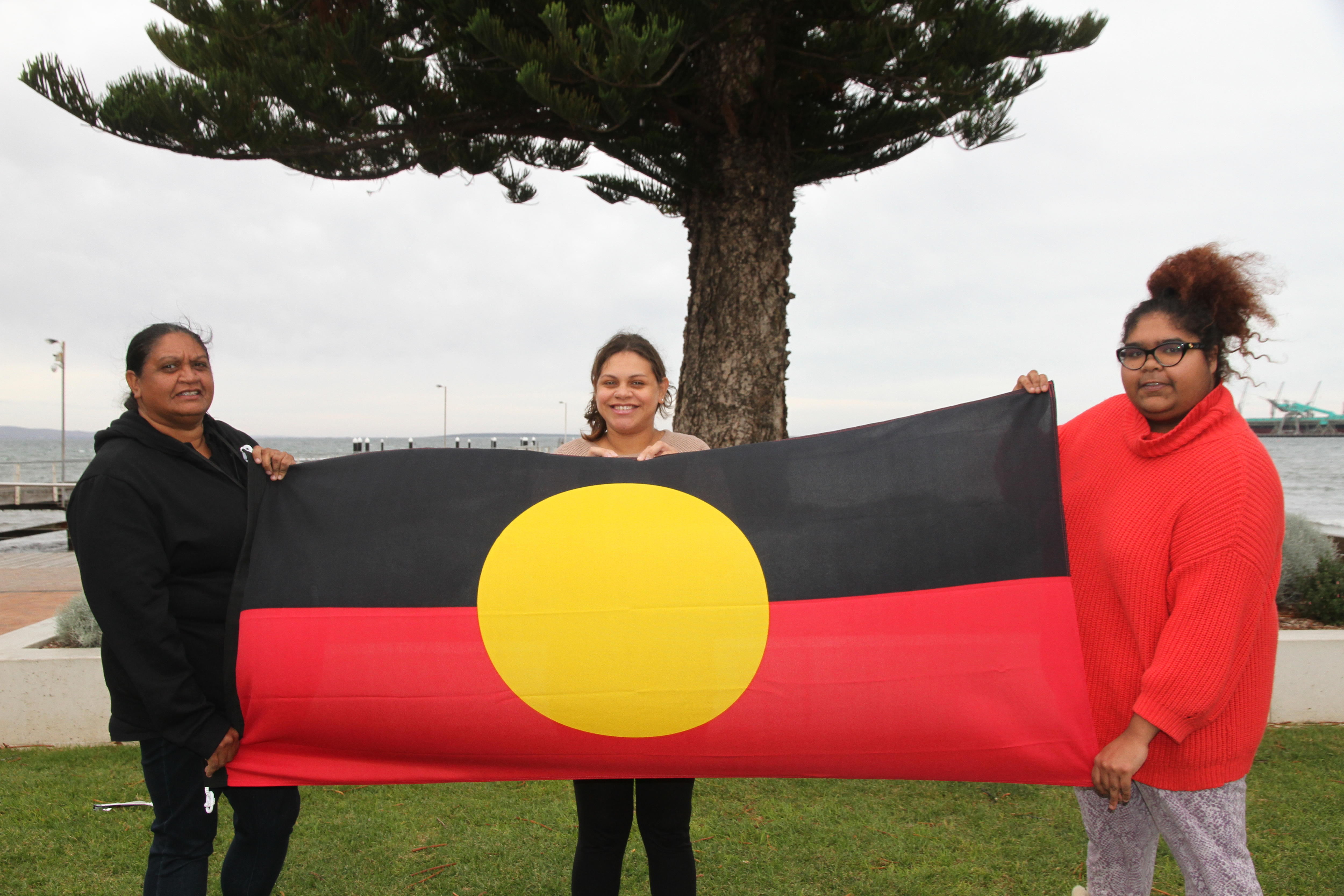 Three family members holding the Aboriginal flag.