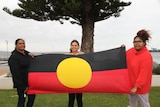 Three family members holding the Aboriginal flag.
