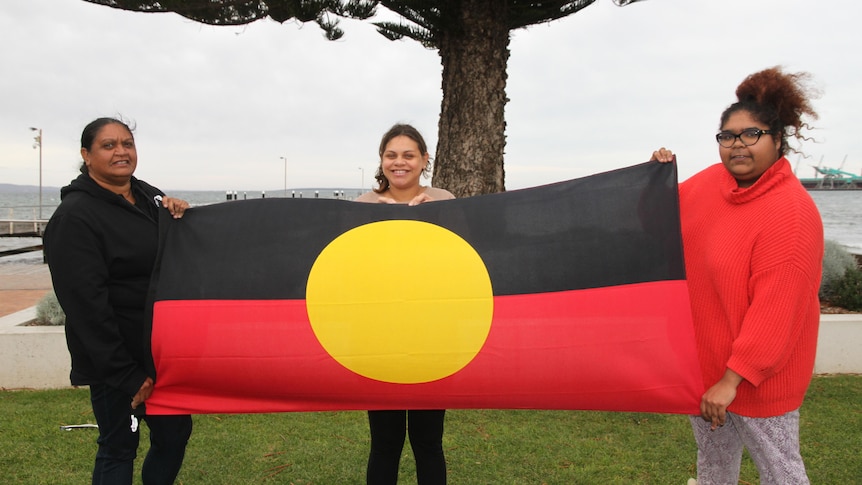 Three family members holding the Aboriginal flag.