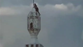far away shot of two figures atop a tall communications tower