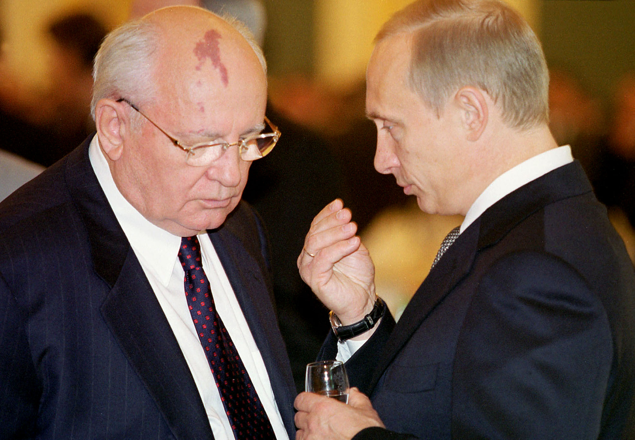 米哈伊尔·戈尔巴乔夫（左）低着头听拿着一杯酒的弗拉基米尔·普京讲话