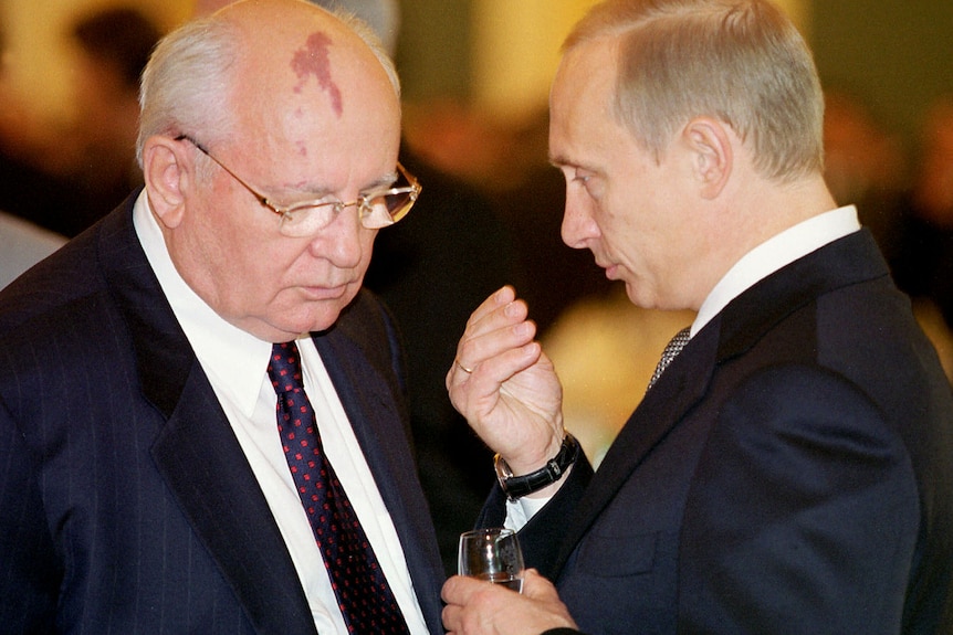 Mikhail Gorbachev (left) with his head bend down listens to Vladimir Putin who holds a glass of wine
