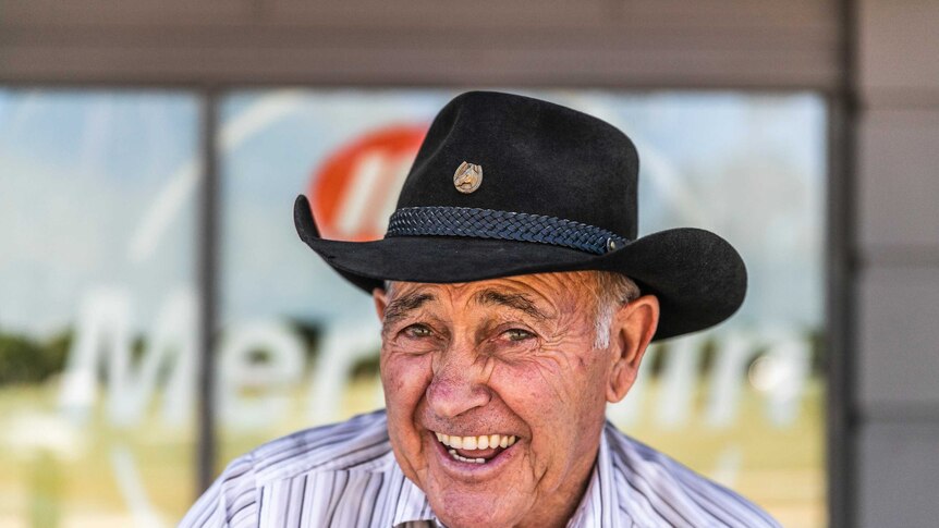 An old man with a cowboy hat on smiles at the camera.
