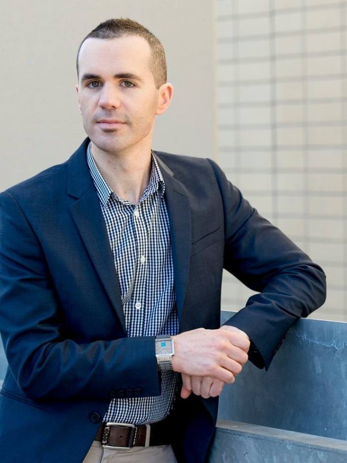 Portrait photo of a man in his thirties with blue eyes and dark hair.