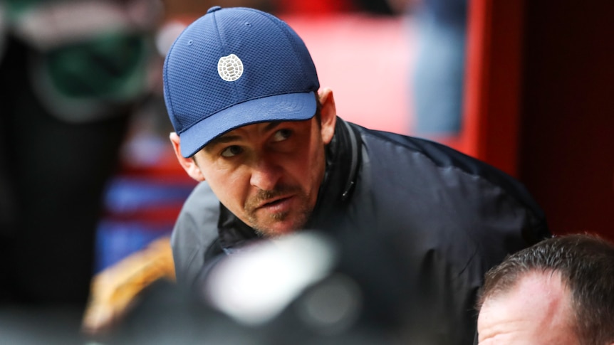 Joey Barton wears a cap while talking on the sidelines at a Bristol Rovers game.