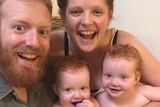 A smiling father and mother hold their twins, dressed in nappies.