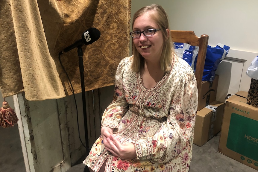 A lady sitting on a chair next to an ABC microphone.