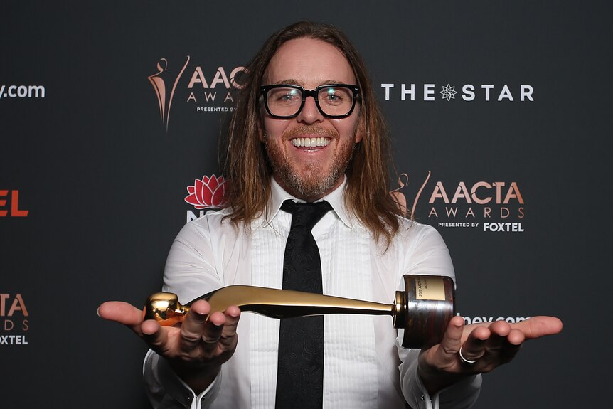 A man holds an award laid horizontally across his hands.