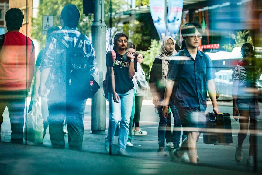 the reflection on a glass mirrored wall of a group of young people walking