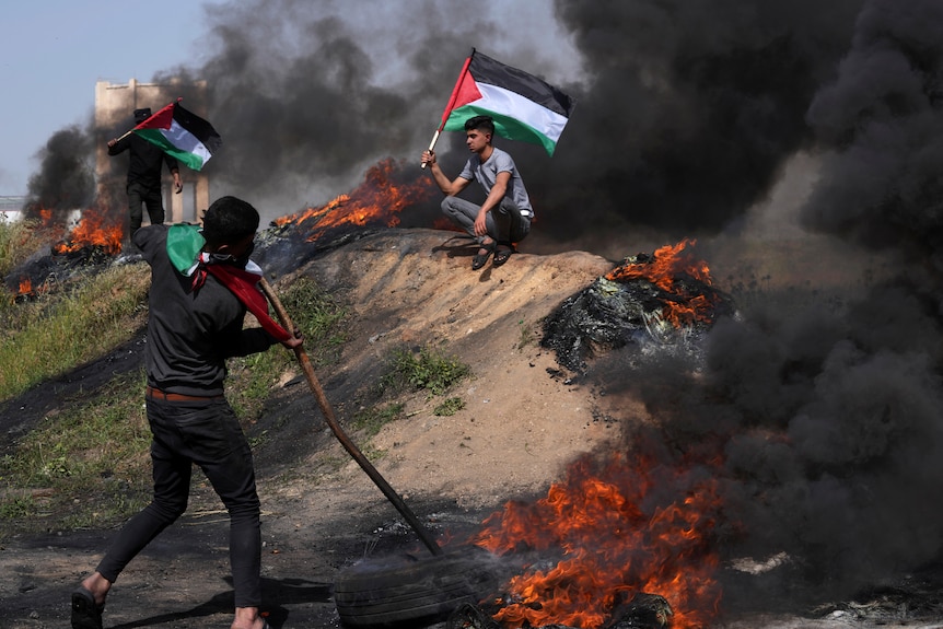 Palestinians burn tires and wave the national flag during a protest in Gaza.
