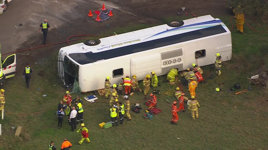 A white bus on its side surrounded by emergency services personnel in high vis.